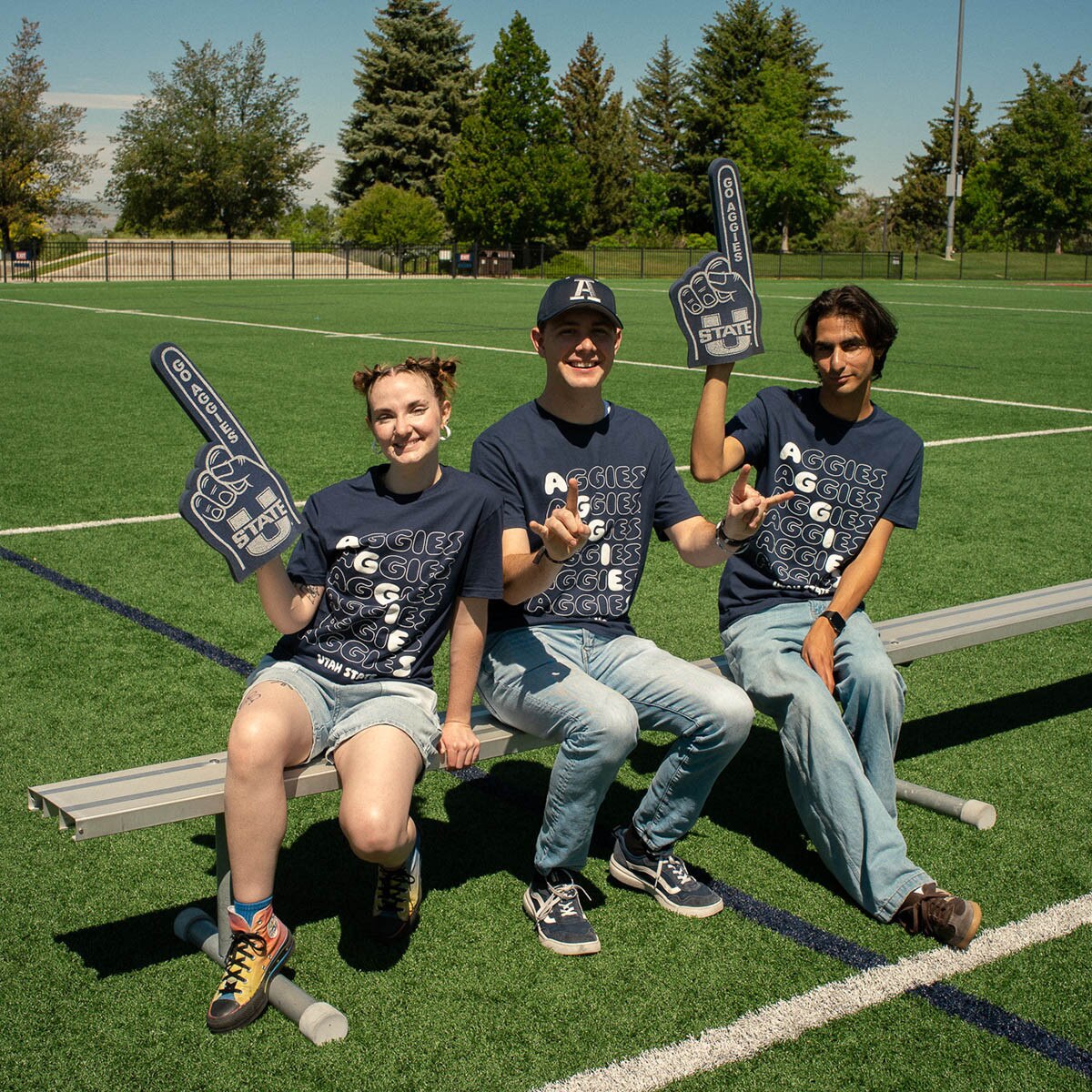 Three students wearing gameday t-shirts with foam fingers cheering on the field